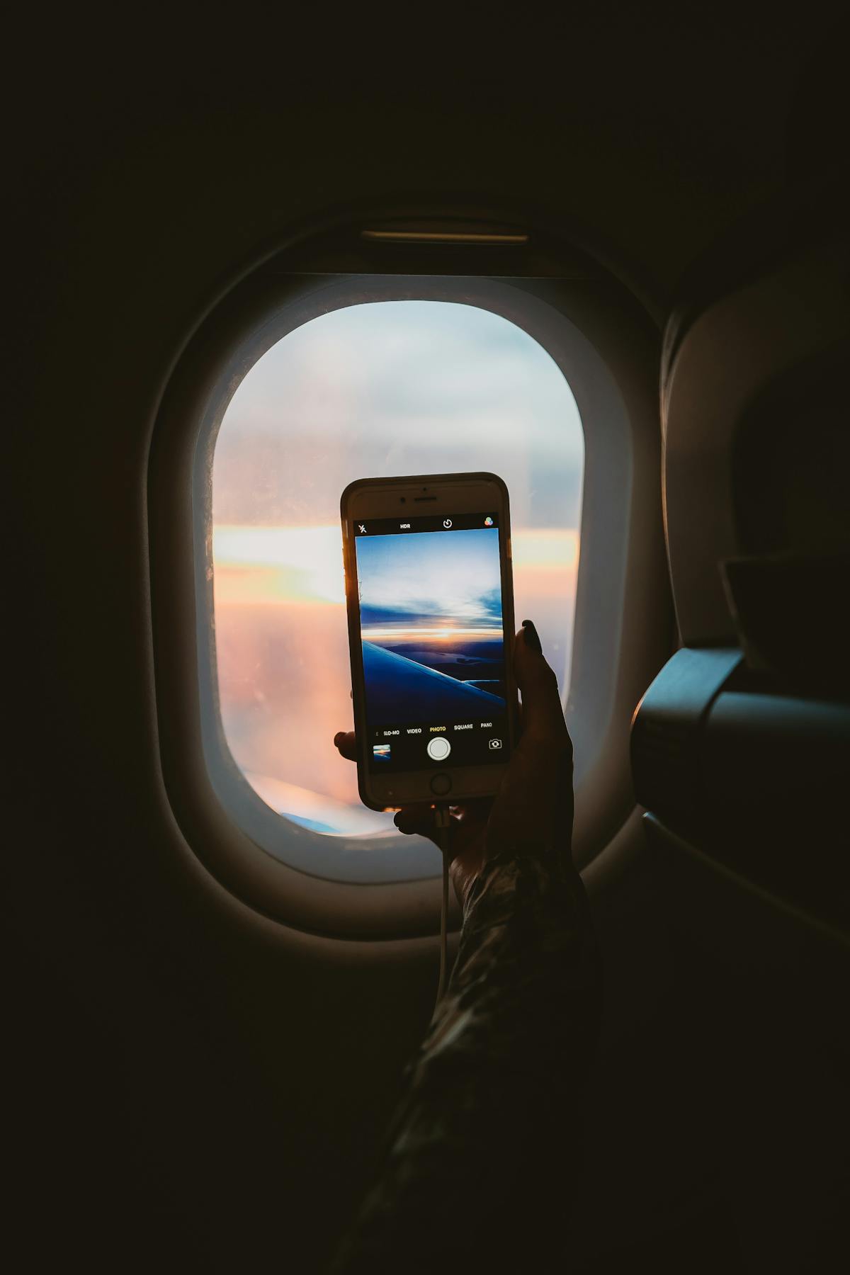 Looking out an airplane window at sunset, holding a phone — the texture of long-distance life.