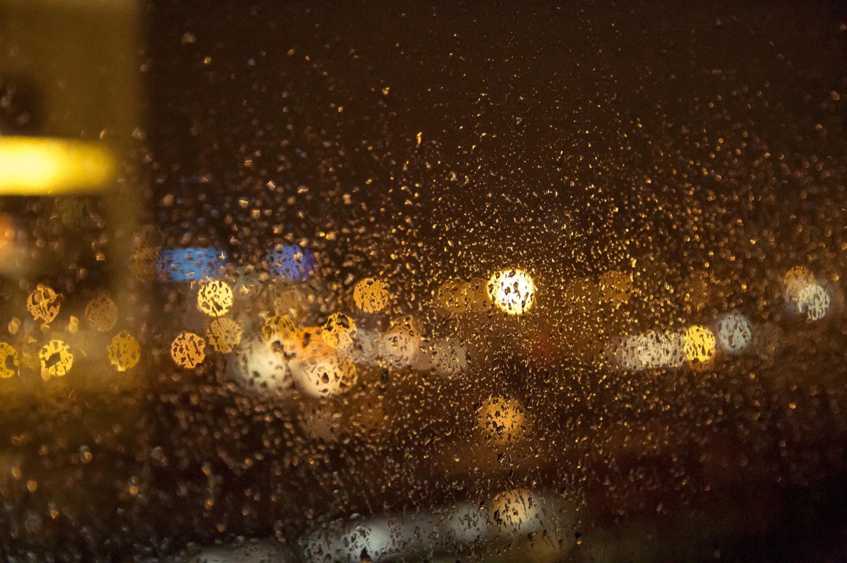Rain running down a dark window at night, with city lights blurred warm behind the glass