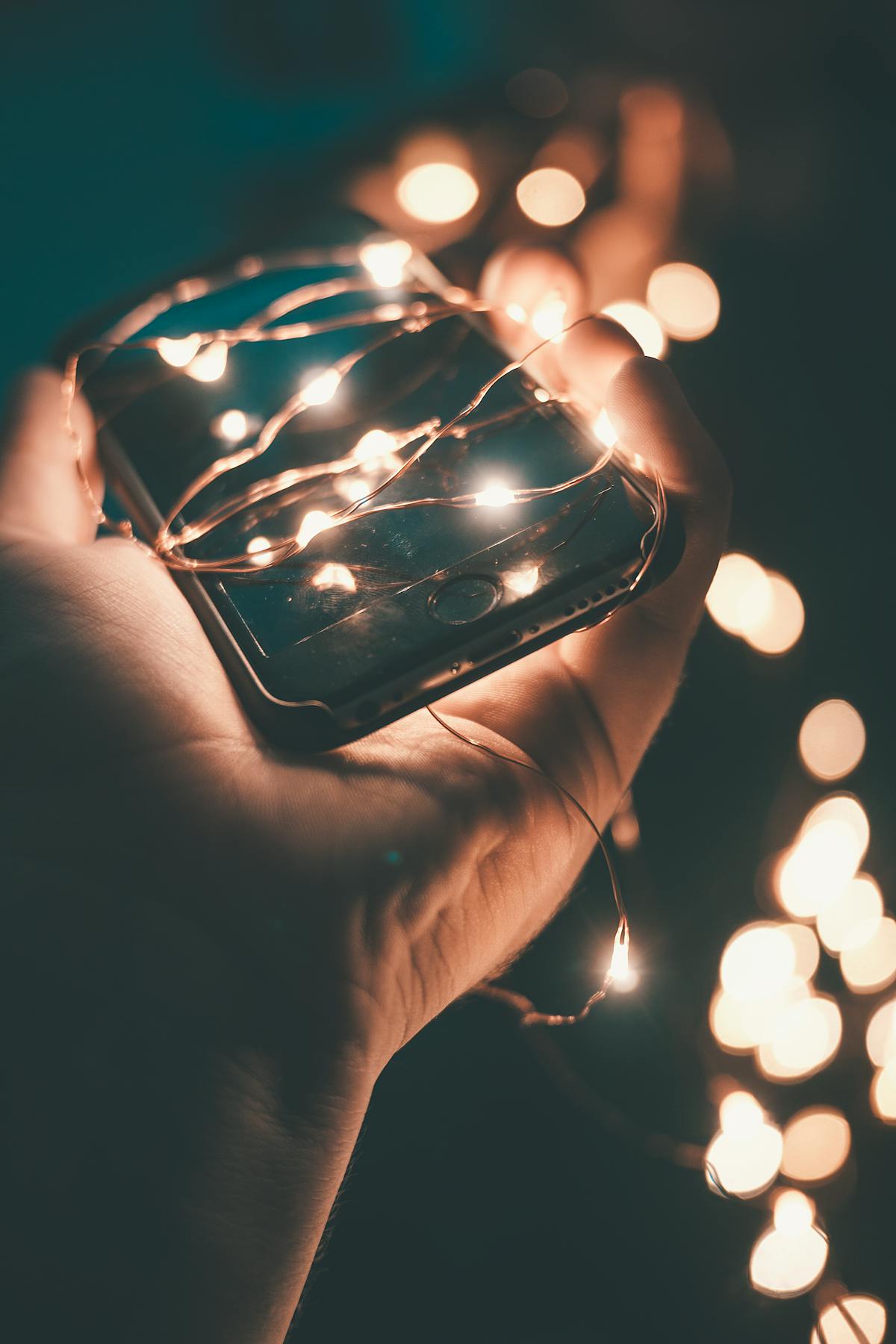 A phone wrapped in warm string lights, held in a hand