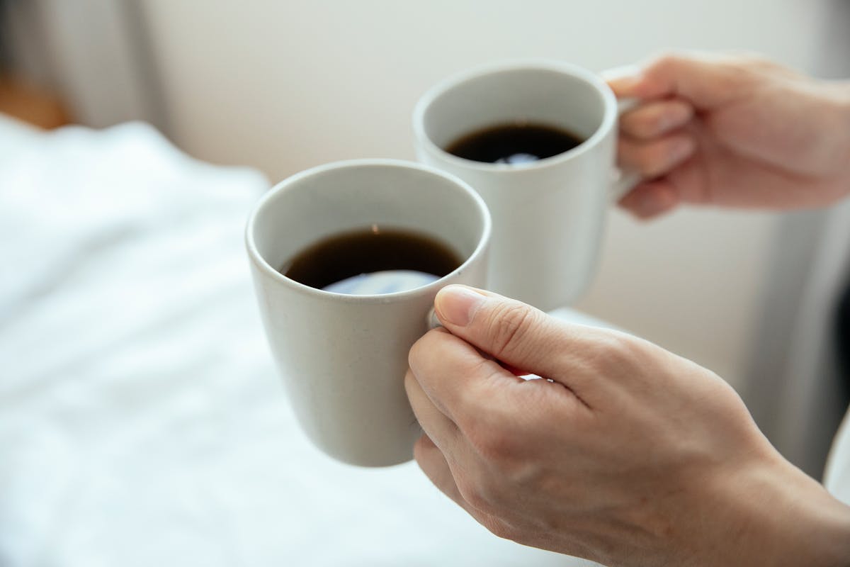 Two hands holding warm mugs of coffee — the kind of moment a small prompt can land in.